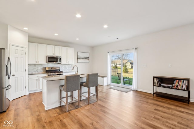 kitchen featuring a breakfast bar, a kitchen island with sink, white cabinets, light hardwood / wood-style flooring, and appliances with stainless steel finishes