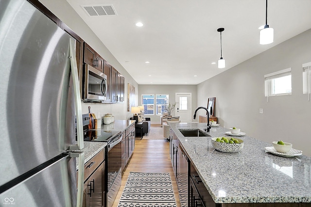 kitchen featuring stainless steel appliances, a spacious island, visible vents, a sink, and dark brown cabinetry