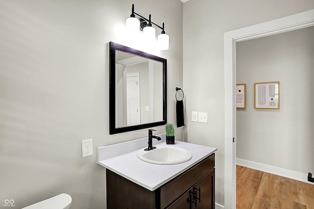 bathroom with toilet, wood finished floors, vanity, and baseboards