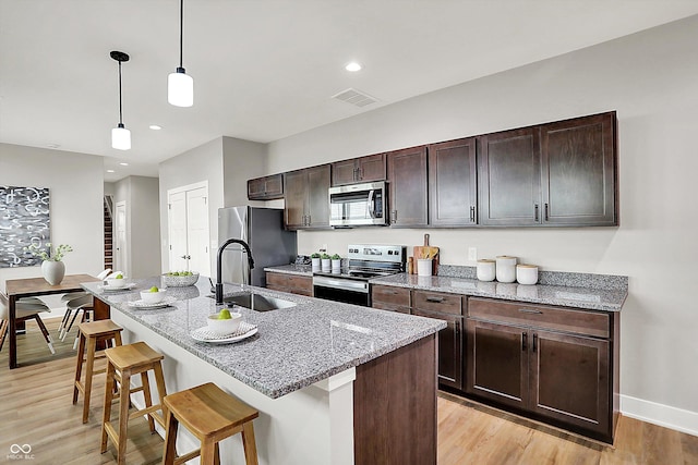 kitchen with a breakfast bar area, appliances with stainless steel finishes, a kitchen island with sink, light wood-type flooring, and a sink