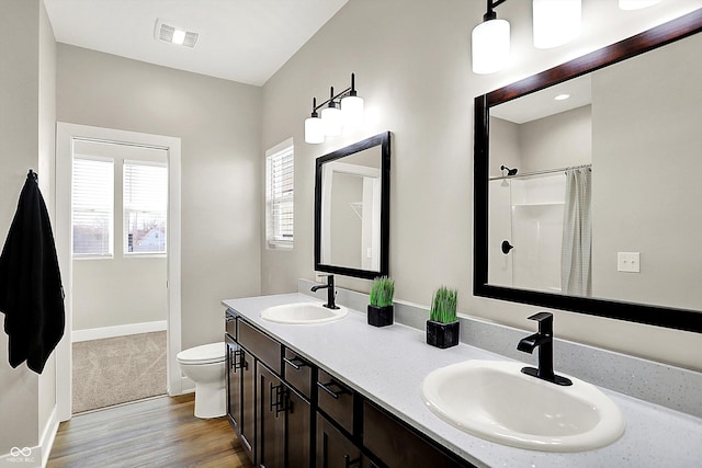 full bath with toilet, visible vents, a sink, and wood finished floors