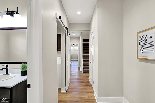 hallway featuring a barn door, recessed lighting, a sink, baseboards, and light wood-type flooring