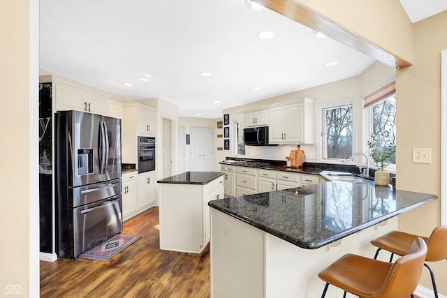 kitchen featuring black appliances, a kitchen island, sink, a kitchen breakfast bar, and kitchen peninsula