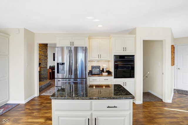 kitchen featuring stainless steel refrigerator with ice dispenser, backsplash, dark wood-type flooring, oven, and dark stone countertops