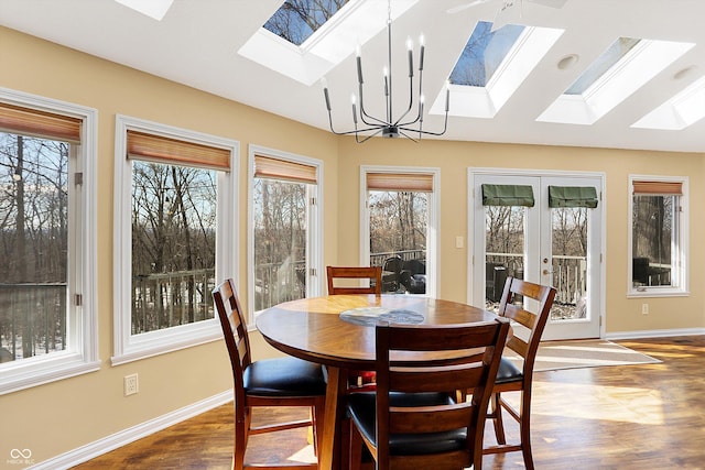 dining room featuring dark wood-type flooring, vaulted ceiling with skylight, french doors, and an inviting chandelier