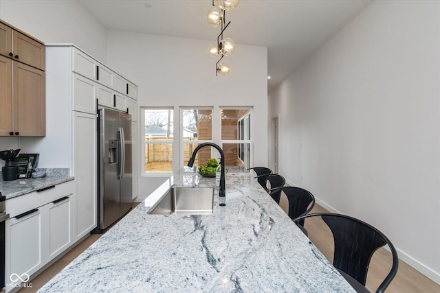 kitchen with stainless steel fridge, light stone counters, and white cabinetry