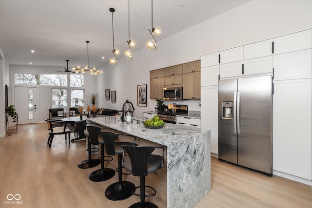 kitchen featuring stainless steel appliances, ceiling fan, a kitchen island with sink, decorative light fixtures, and white cabinets