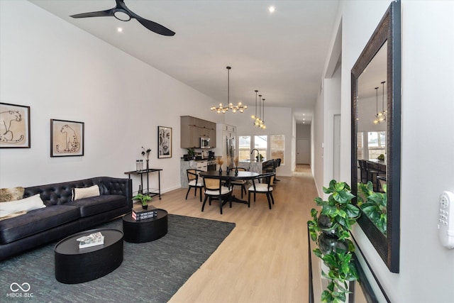 living room with ceiling fan with notable chandelier and light hardwood / wood-style flooring