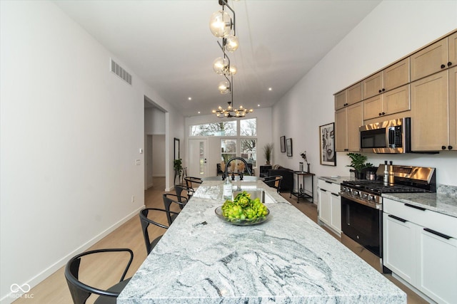 kitchen with a large island with sink, an inviting chandelier, sink, appliances with stainless steel finishes, and light stone counters