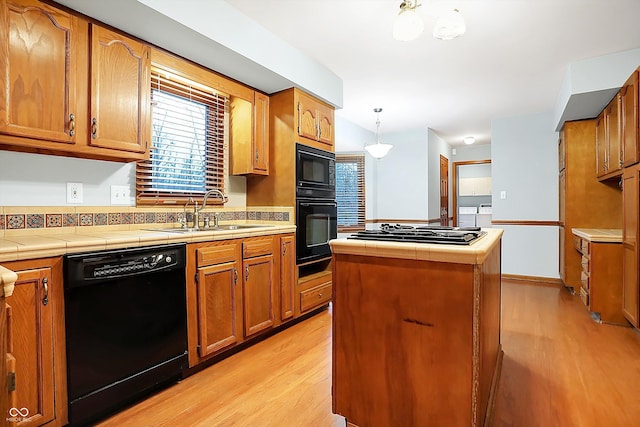 kitchen with tile countertops, a center island, black appliances, sink, and hanging light fixtures