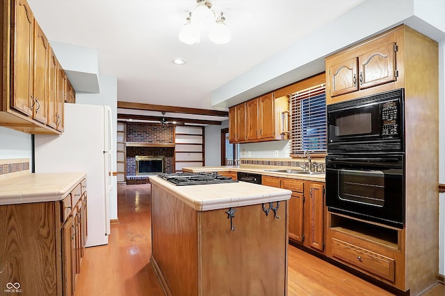 kitchen with tile counters, sink, light hardwood / wood-style floors, a kitchen island, and black appliances