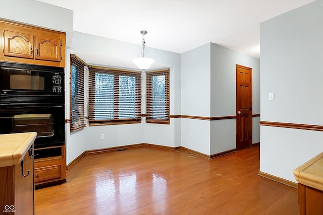 interior space with black appliances, tile counters, pendant lighting, and light hardwood / wood-style floors