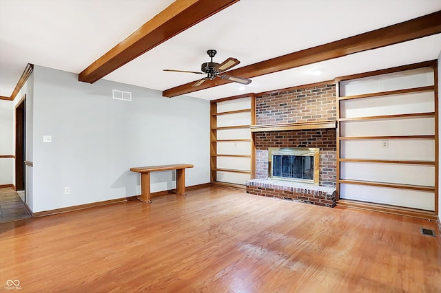 unfurnished living room featuring beamed ceiling, ceiling fan, light wood-type flooring, and a brick fireplace