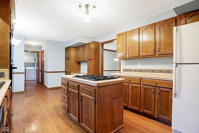 kitchen featuring a center island, stainless steel gas cooktop, light hardwood / wood-style flooring, white fridge, and washer / dryer