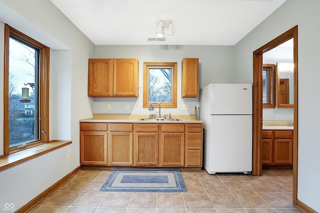 kitchen with light tile patterned flooring, white refrigerator, and sink