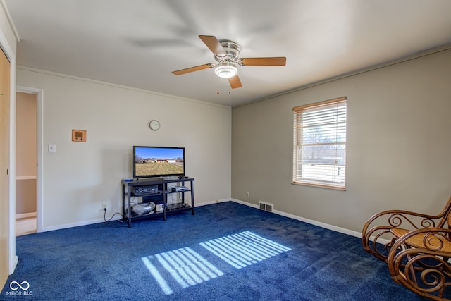 living area with ceiling fan, ornamental molding, and dark colored carpet