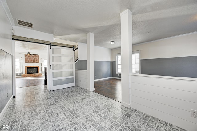 unfurnished room with a textured ceiling, ornamental molding, a fireplace, and a barn door