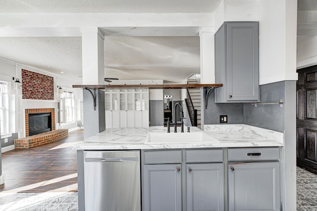 kitchen with gray cabinetry, a fireplace, dishwasher, a textured ceiling, and sink