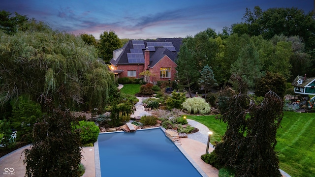 pool at dusk featuring a lawn and a patio