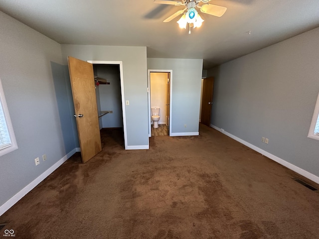 unfurnished bedroom featuring connected bathroom, ceiling fan, dark carpet, and a spacious closet