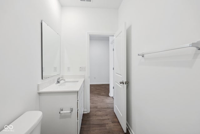 half bathroom featuring visible vents, baseboards, toilet, wood finished floors, and vanity