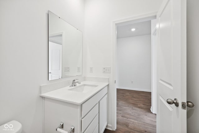 half bathroom with baseboards, toilet, wood finished floors, and vanity