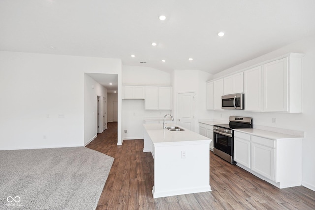 kitchen with an island with sink, a sink, wood finished floors, appliances with stainless steel finishes, and vaulted ceiling