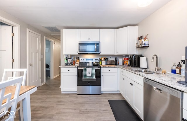 kitchen with sink, stainless steel appliances, light stone counters, white cabinets, and light wood-type flooring