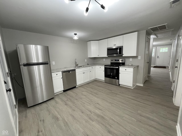 kitchen with light stone countertops, white cabinetry, sink, stainless steel appliances, and light wood-type flooring