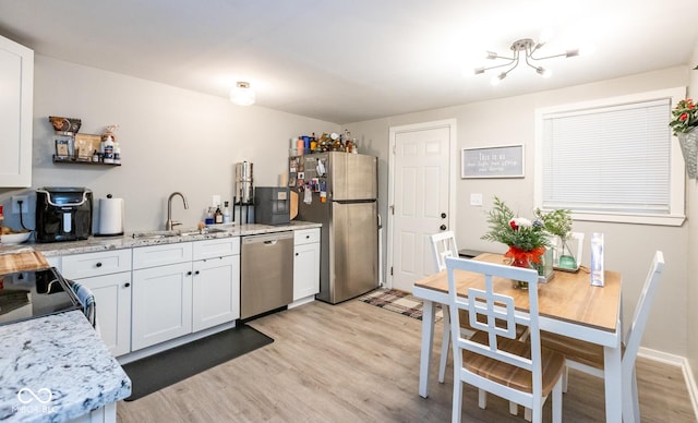 kitchen with white cabinetry, sink, stainless steel appliances, light stone counters, and light hardwood / wood-style floors