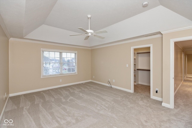 unfurnished bedroom with a walk in closet, ornamental molding, a tray ceiling, ceiling fan, and a closet