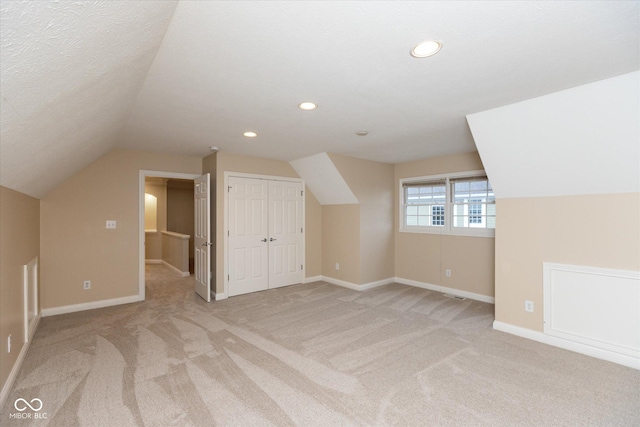 additional living space featuring a textured ceiling, lofted ceiling, and light carpet