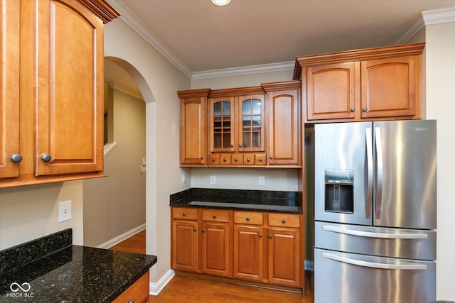 kitchen with stainless steel fridge, dark stone counters, crown molding, and light hardwood / wood-style floors