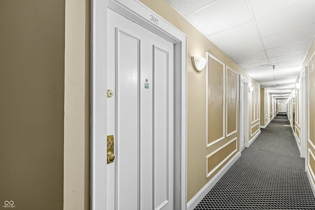 hall with dark colored carpet and a paneled ceiling