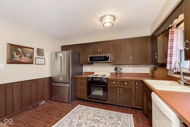 kitchen featuring dark brown cabinetry, wooden walls, sink, and stainless steel appliances