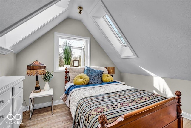 bedroom featuring lofted ceiling with skylight, light hardwood / wood-style flooring, and a textured ceiling