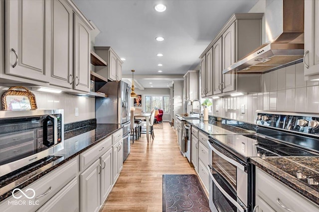 kitchen featuring dark stone counters, wall chimney range hood, gray cabinets, appliances with stainless steel finishes, and light hardwood / wood-style floors