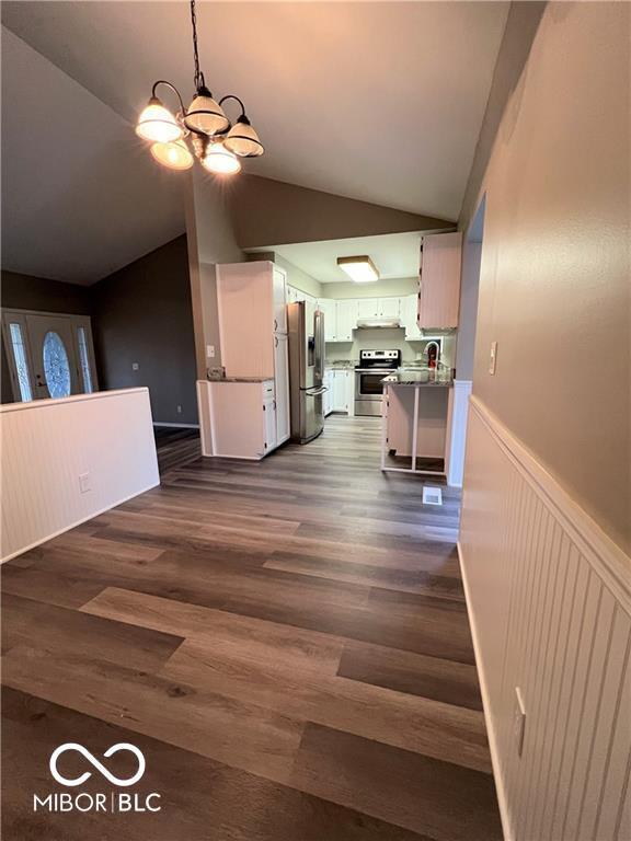 kitchen featuring appliances with stainless steel finishes, dark hardwood / wood-style flooring, vaulted ceiling, a notable chandelier, and white cabinetry