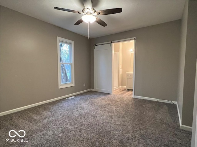 unfurnished bedroom with a barn door, ceiling fan, carpet, and ensuite bath