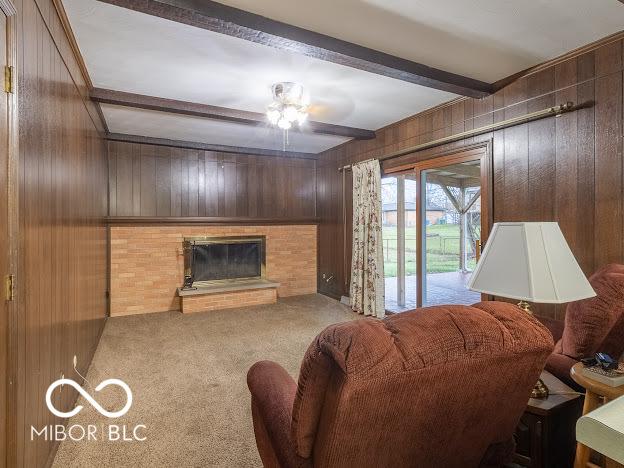 living room featuring wooden walls, ceiling fan, a fireplace, beam ceiling, and light colored carpet