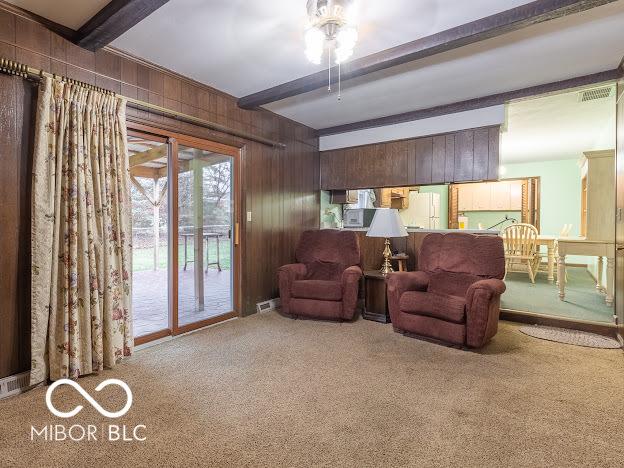 living area with beamed ceiling, ceiling fan, wood walls, and carpet