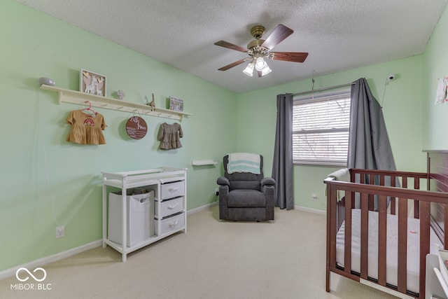 bedroom featuring ceiling fan, a nursery area, carpet floors, and a textured ceiling