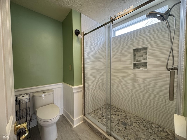 bathroom featuring tile patterned flooring, toilet, a shower with door, and a textured ceiling