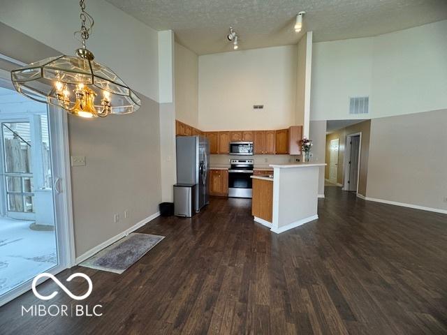 kitchen featuring a notable chandelier, kitchen peninsula, a towering ceiling, a textured ceiling, and appliances with stainless steel finishes