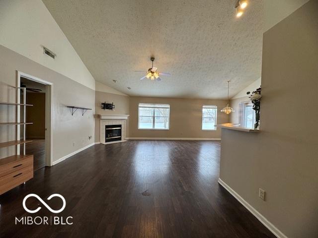 unfurnished living room with a tile fireplace, a textured ceiling, vaulted ceiling, and ceiling fan with notable chandelier