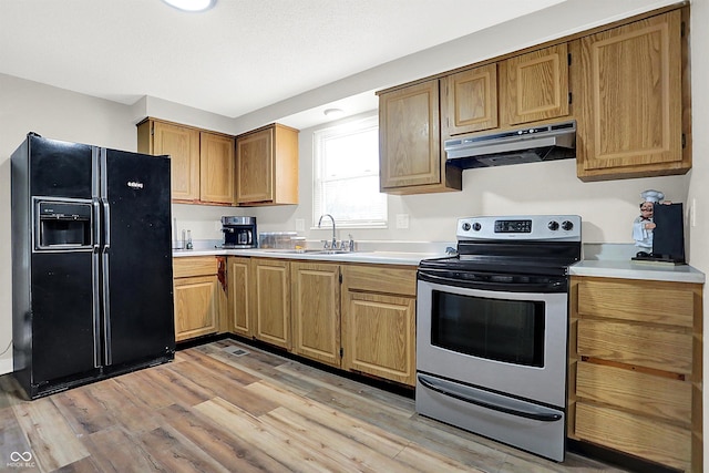 kitchen with light wood-type flooring, black fridge, stainless steel range with electric cooktop, and sink