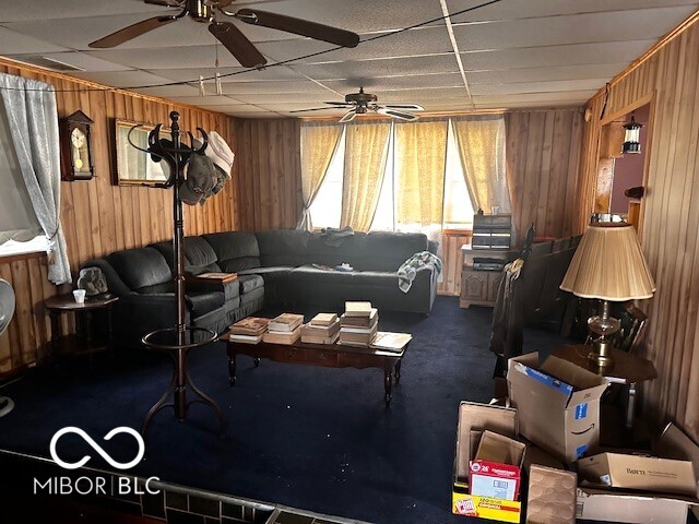 living room featuring wood walls, a drop ceiling, and dark colored carpet