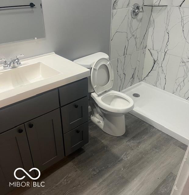 bathroom with hardwood / wood-style flooring, vanity, toilet, and tiled shower