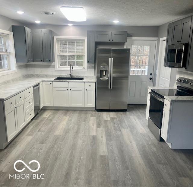 kitchen with gray cabinetry, sink, a textured ceiling, appliances with stainless steel finishes, and light hardwood / wood-style floors