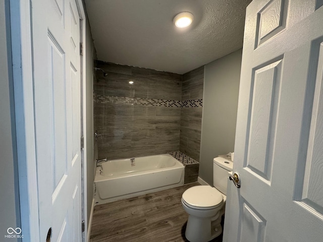 bathroom with hardwood / wood-style flooring, toilet, a textured ceiling, and tiled shower / bath